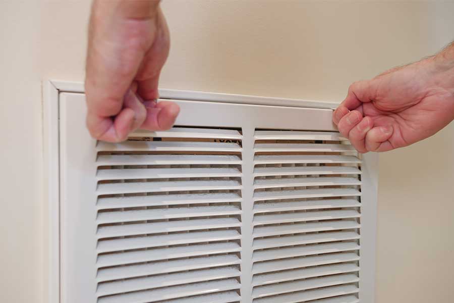 Hands opening an air return vent cover on a wall