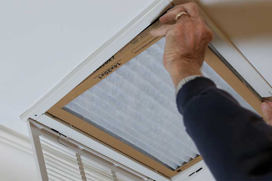 Person replacing an HVAC air filter in a ceiling vent.