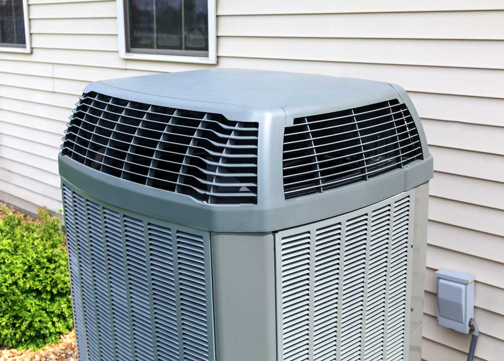 Close-up of an outdoor air conditioning unit next to a house with beige siding