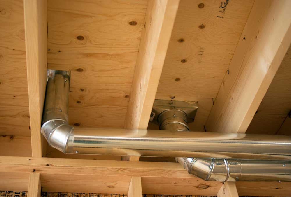 Metal air duct installed between wooden ceiling joists