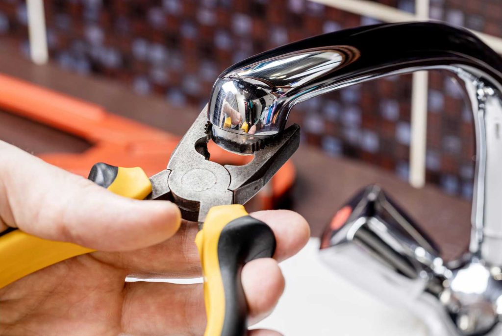 Hand using pliers to fix a chrome kitchen faucet