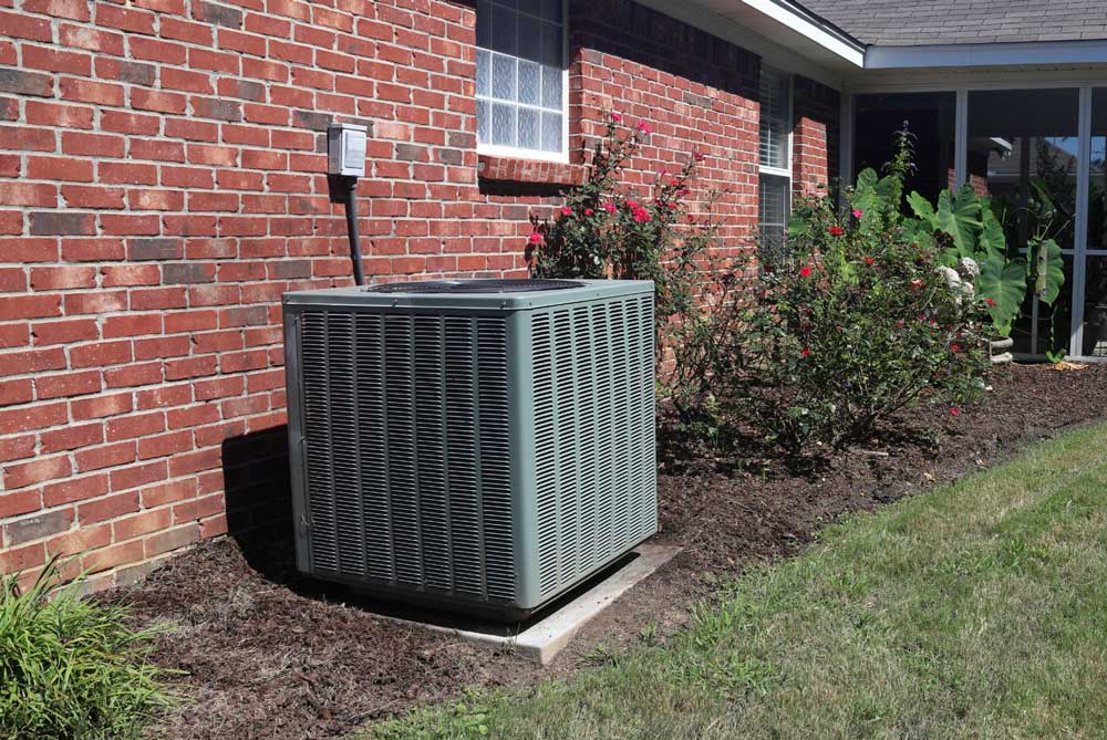 Outdoor air conditioning unit installed beside a brick house with landscaping