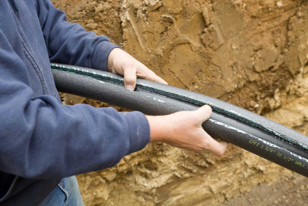Worker holding a partially insulated underground piping system at a construction site