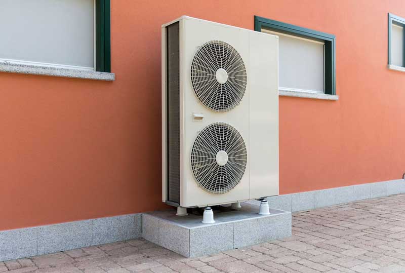 Dual-fan outdoor heat pump unit installed against a building wall