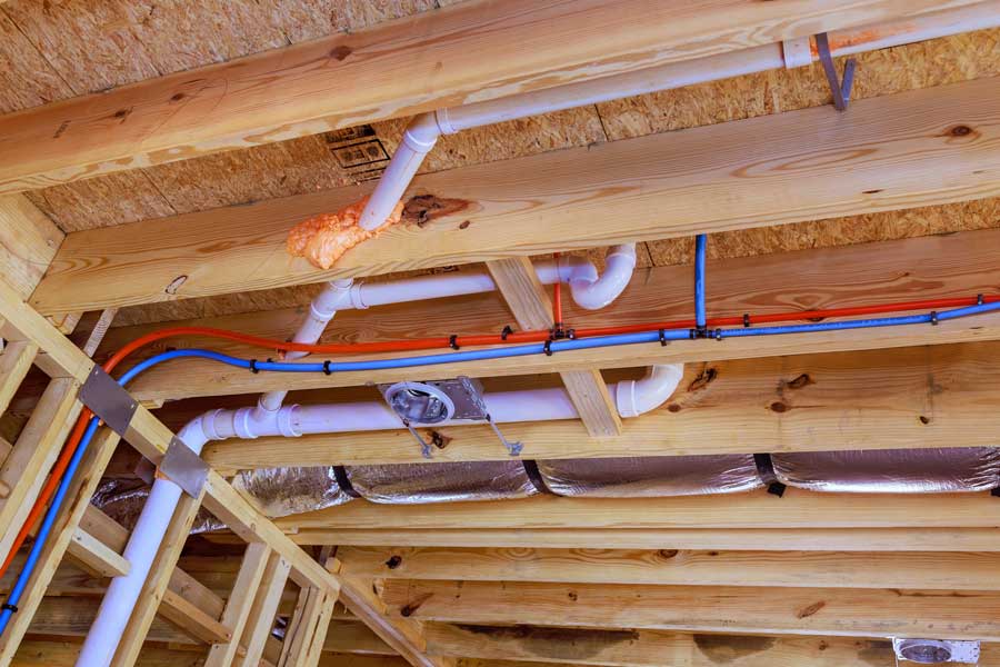 Pipes and conduits installed between wooden ceiling joists of a building.