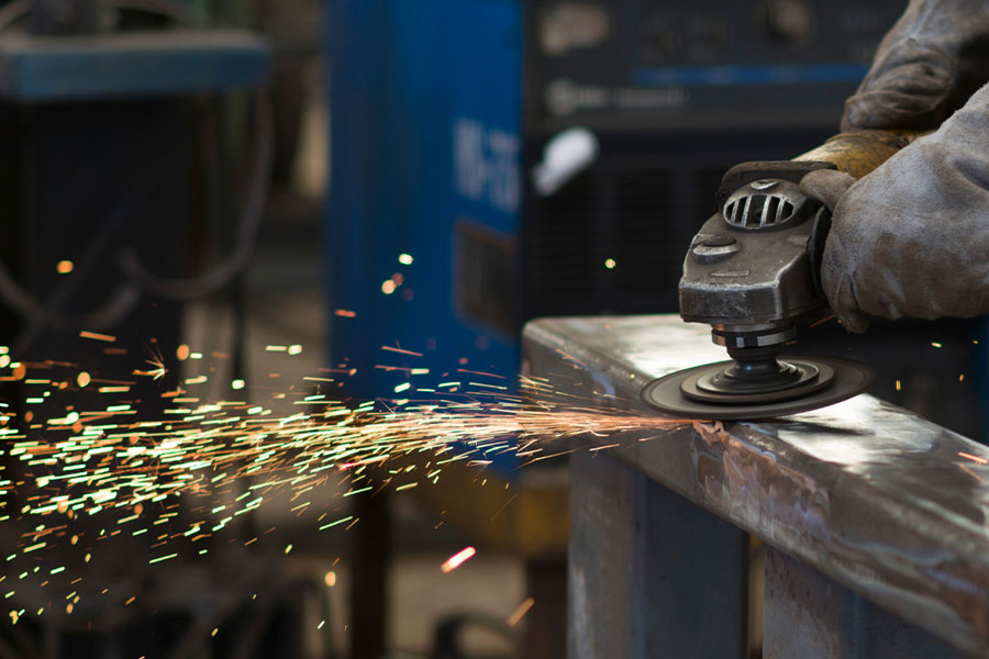 A worker using an angle grinder on a metal surface, producing bright sparks.