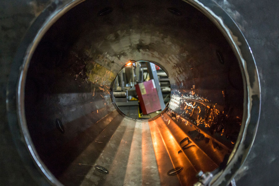 Inside view of a large industrial metal pipe with a circular opening, reflecting ambient light.