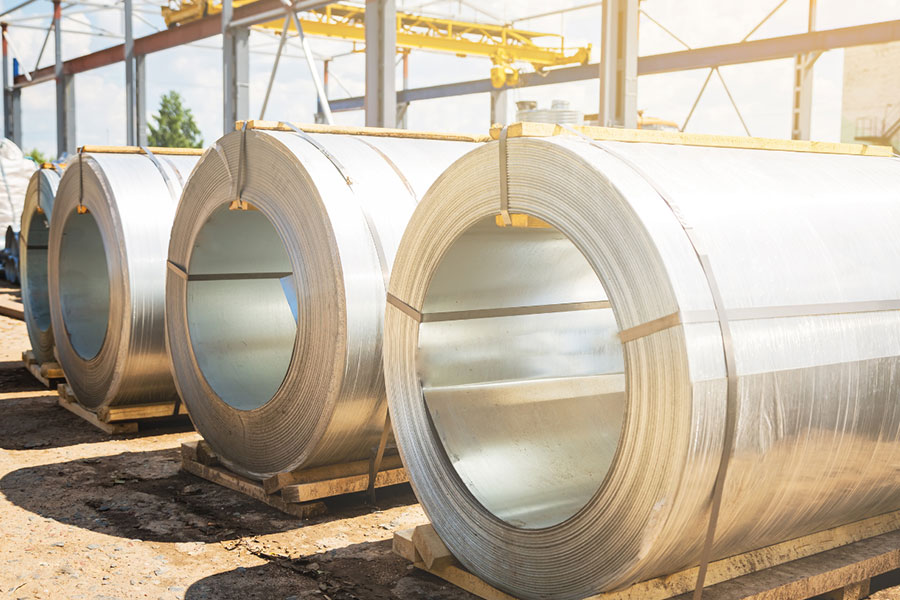 Large galvanized steel coils neatly stacked on wooden pallets at an outdoor industrial site