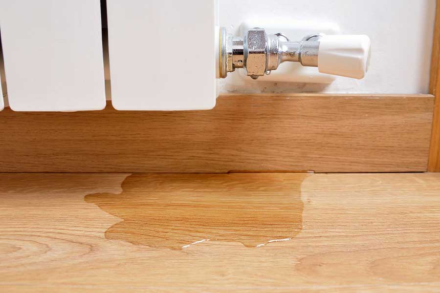 Leaking radiator valve with water pooling on a wooden floor