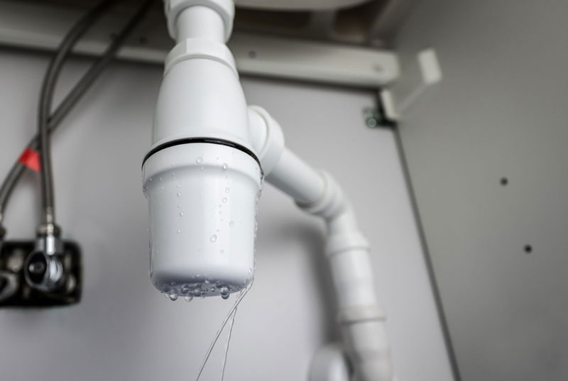 Leaking white plastic P-trap pipe under a sink with dripping water