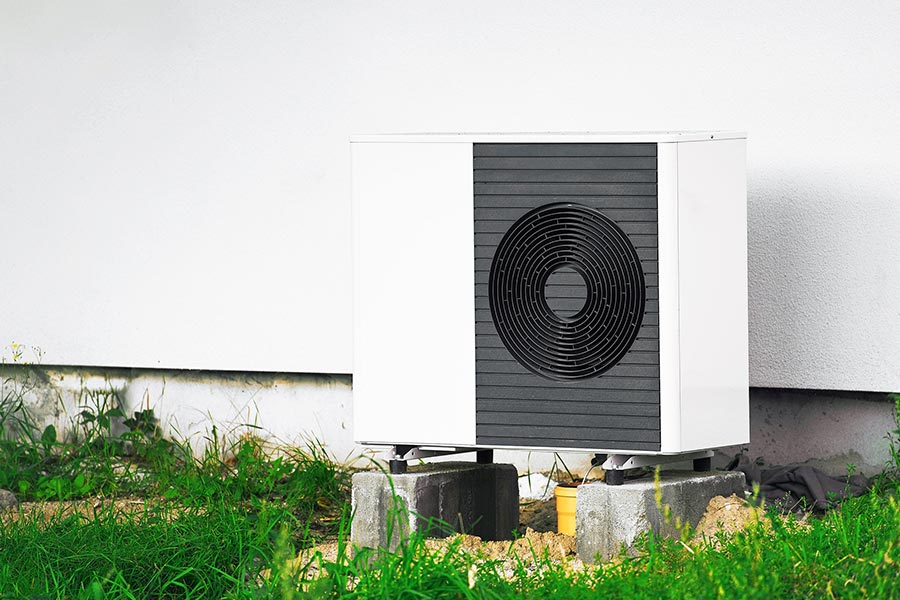 Outdoor heat pump unit installed on concrete blocks against a white wall