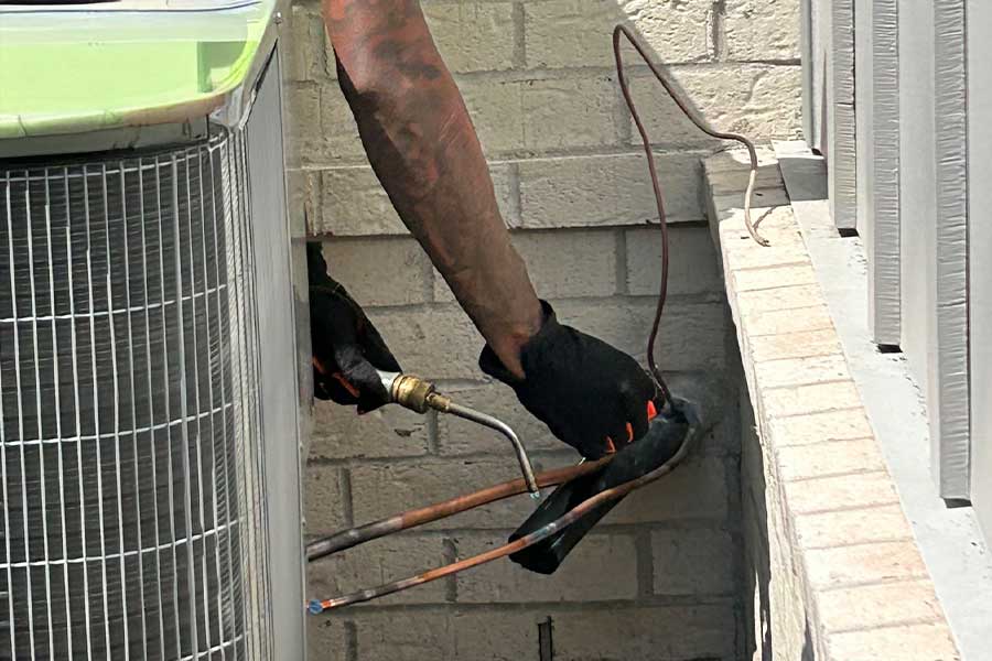 A worker performing a brazing repair on AC refrigerant lines outdoors