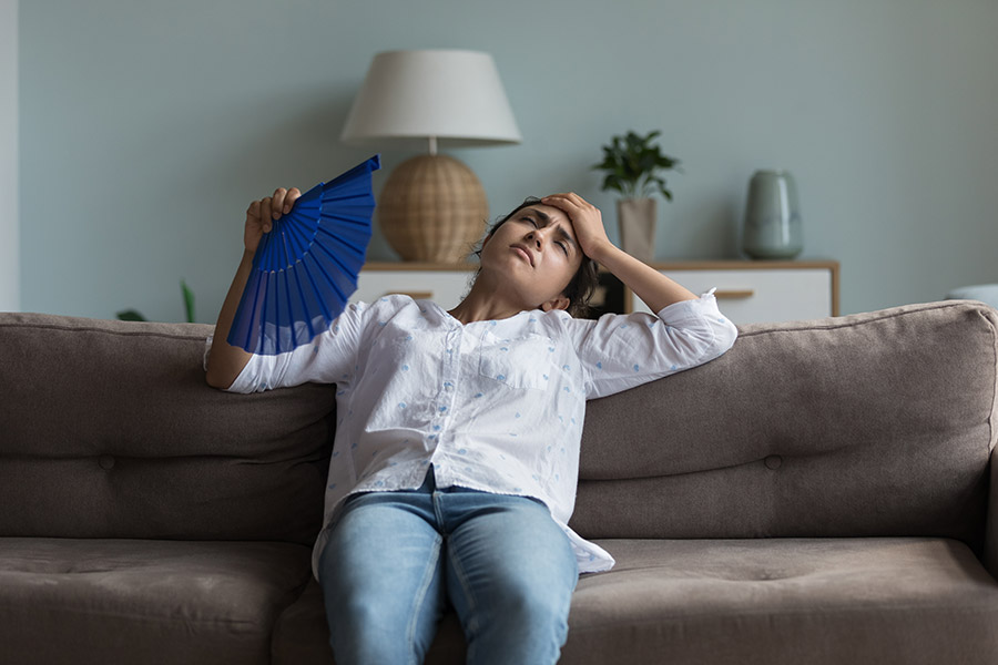 Woman struggling with heat, fanning herself on a couch